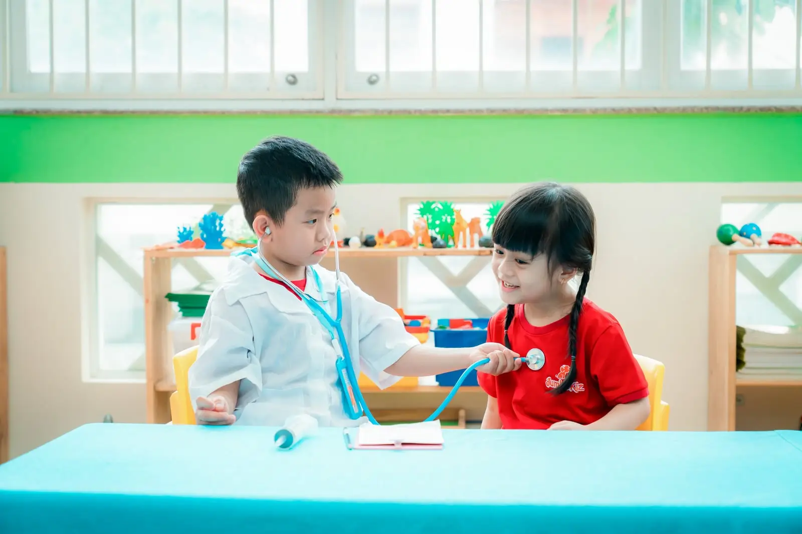 Bé trai đóng vai bác sĩ, dùng ống nghe khám cho bạn gái ở góc chơi