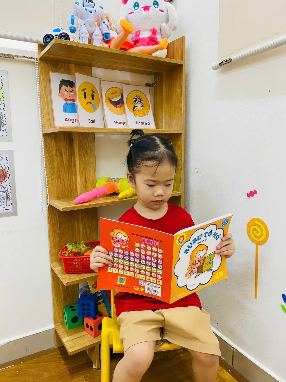 Bé gái lớp K1 ngồi đọc sách ở góc bình tĩnh có thẻ cảm xúc