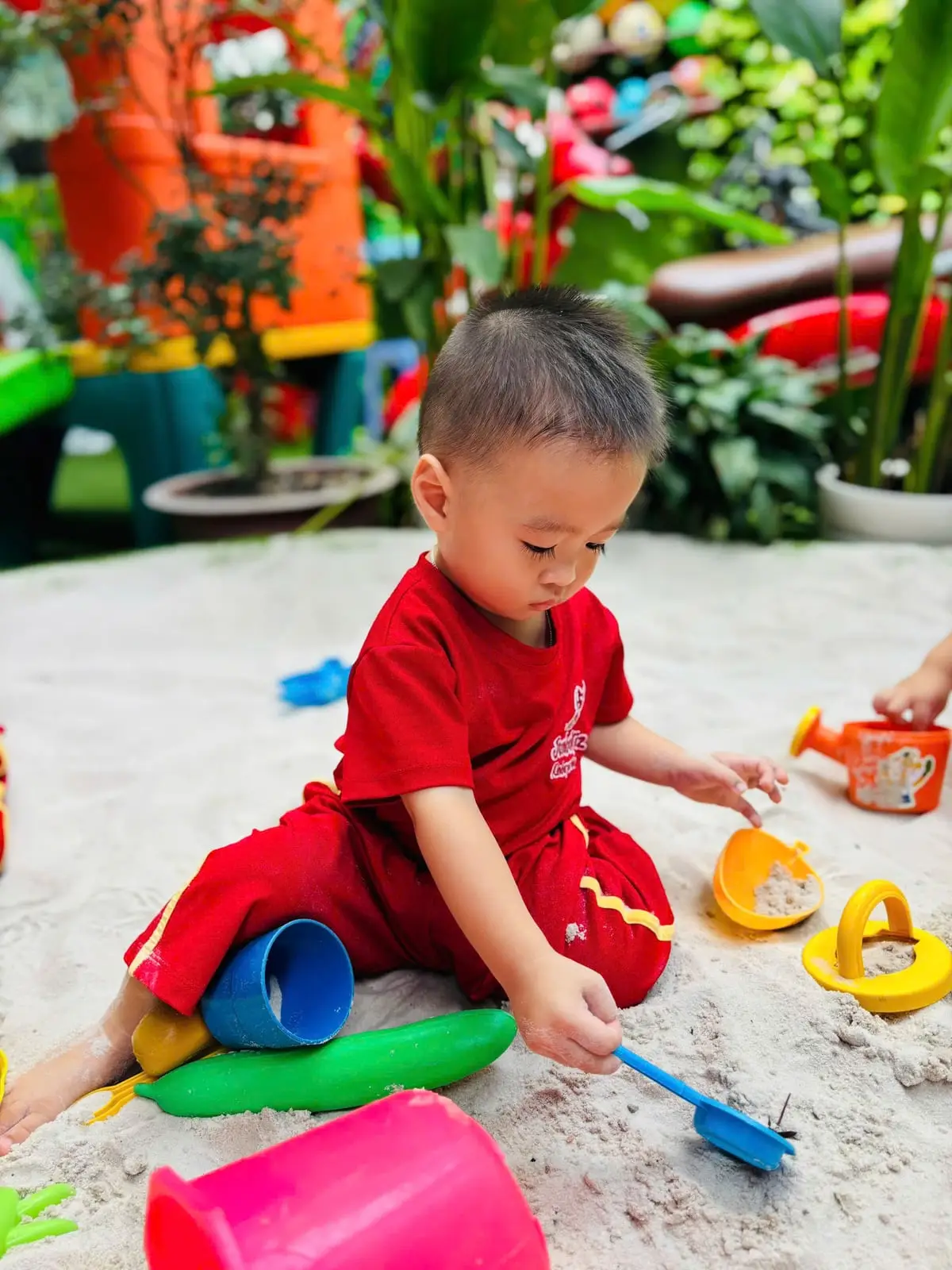 Bé trai lớp PreK1 chăm chú xúc cát vào khuôn trong giờ Jumbo Gym ở nhà trẻ
