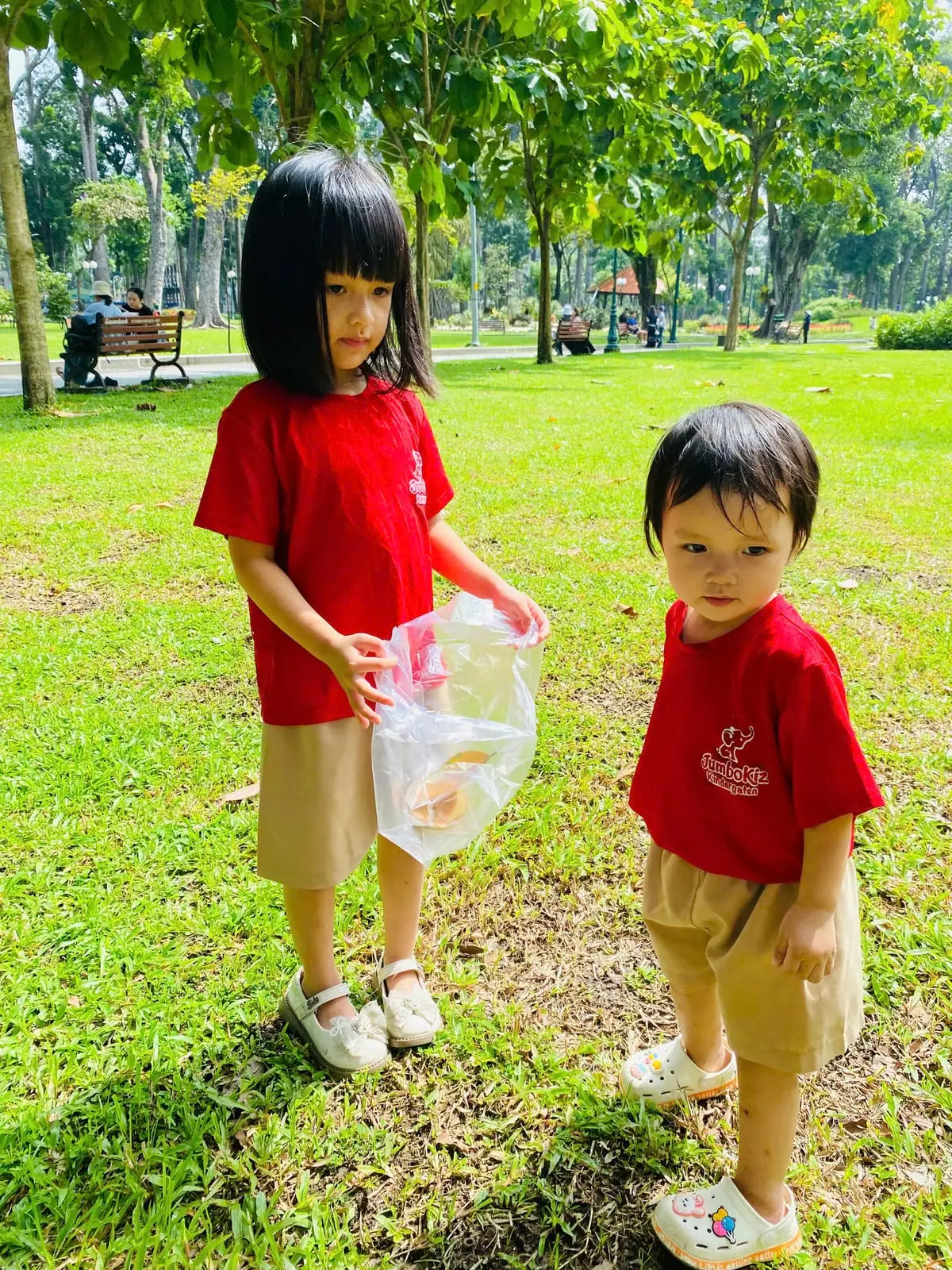 Hai bé cùng nhặt lá trên bãi cỏ trong buổi dã ngoại