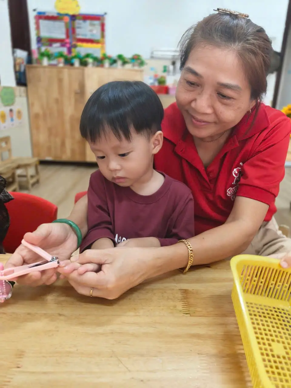 Cô giáo ôm bé trai lớp PreK2A vào lòng cắt móng tay cho bé