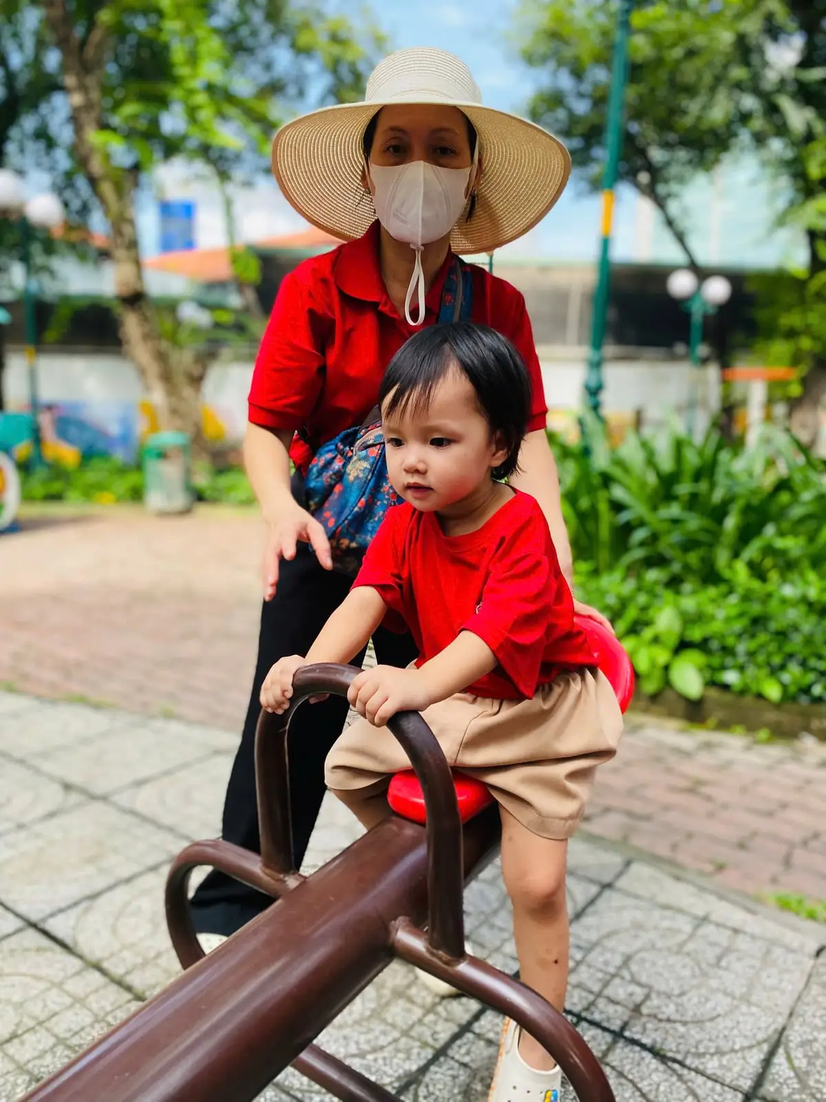 Cô đội nón đỡ bé ngồi bập bênh ở công viên trong buổi dã ngoại
