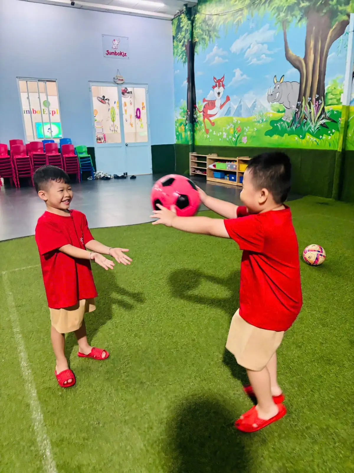 Hai bé trai cười, chuyền bóng cho nhau trên sân cỏ ở JumboKiz