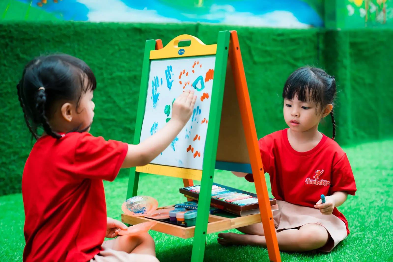 Hai bé gái cùng vẽ bằng tay lên giá vẽ trên sân cỏ