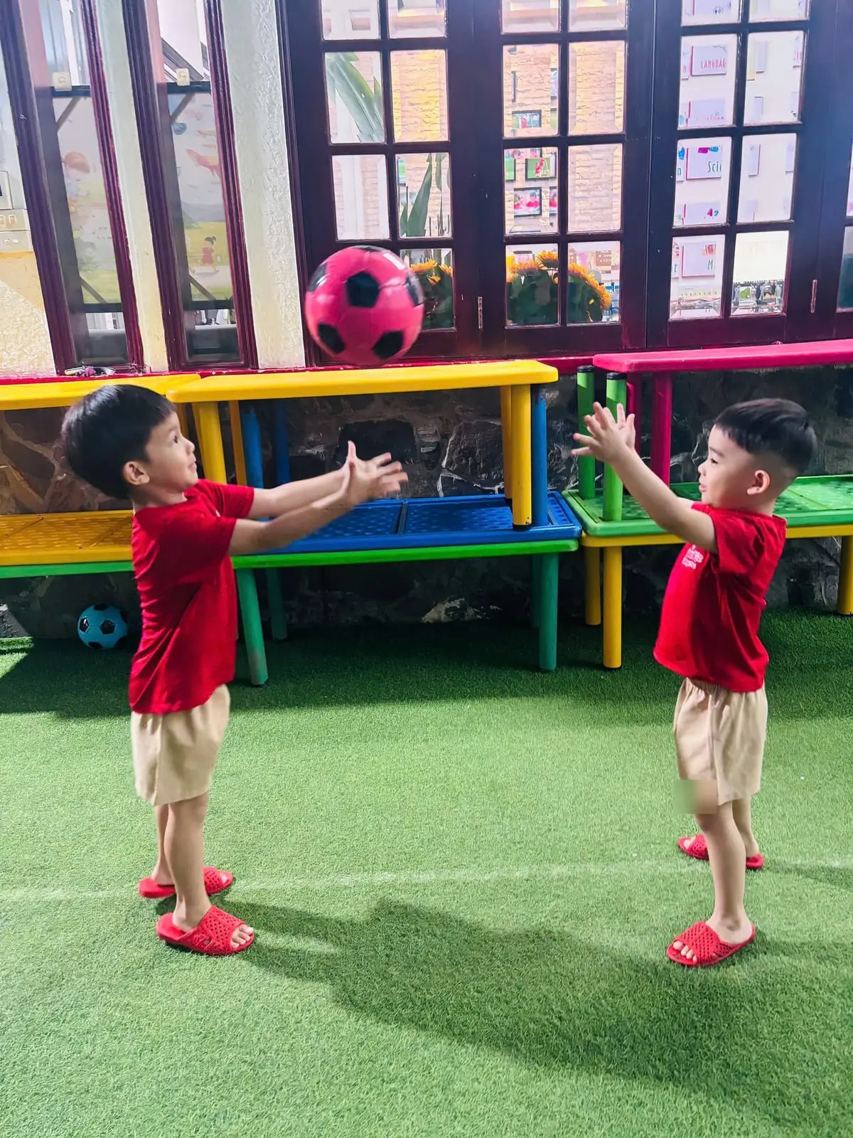 Hai bé trai đứng đối diện tung bắt quả bóng hồng trên sân cỏ