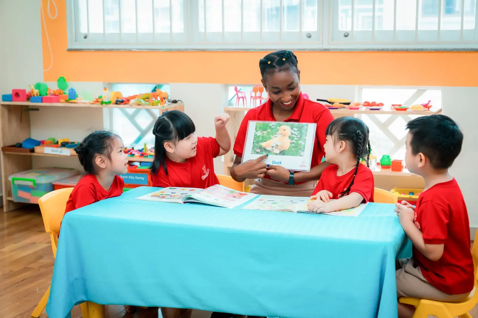 Cô giáo nước ngoài giơ thẻ hình con vịt cho bốn bé quanh bàn