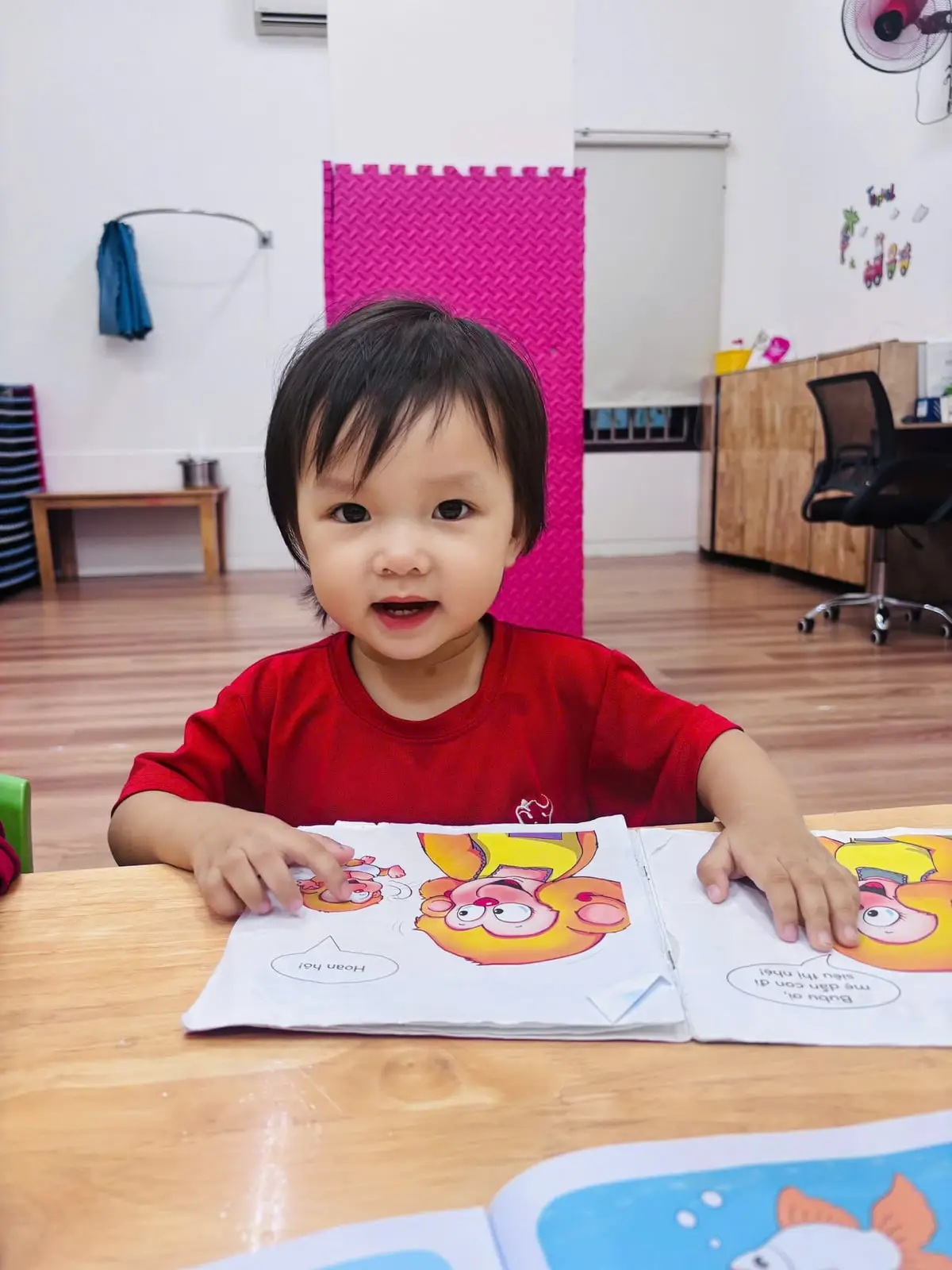 Bé gái lớp Chồi K2 cười tươi bên cuốn truyện tranh đang mở