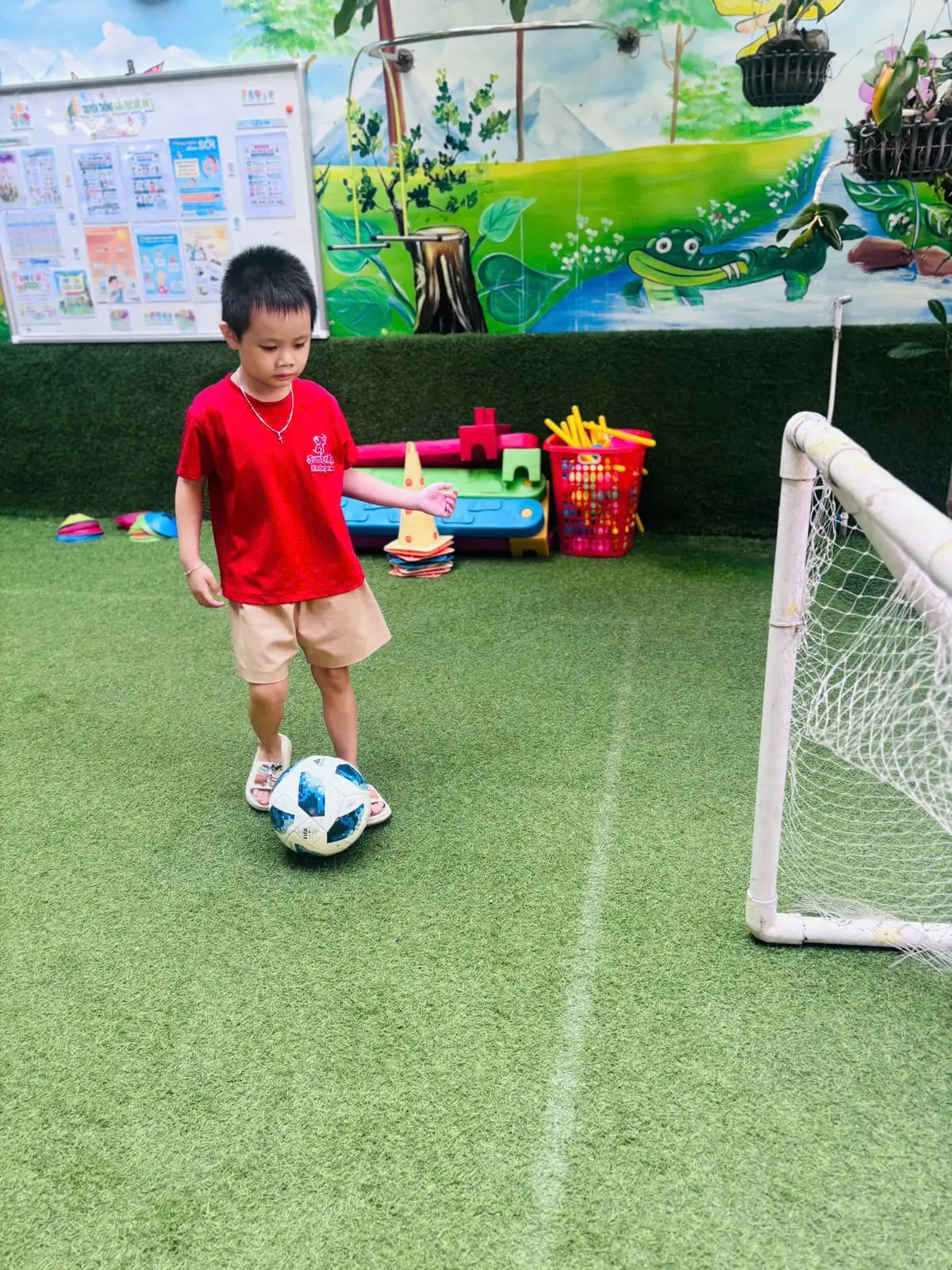 Bé trai lớp Chồi K2 dẫn bóng về phía khung thành mini trên sân cỏ