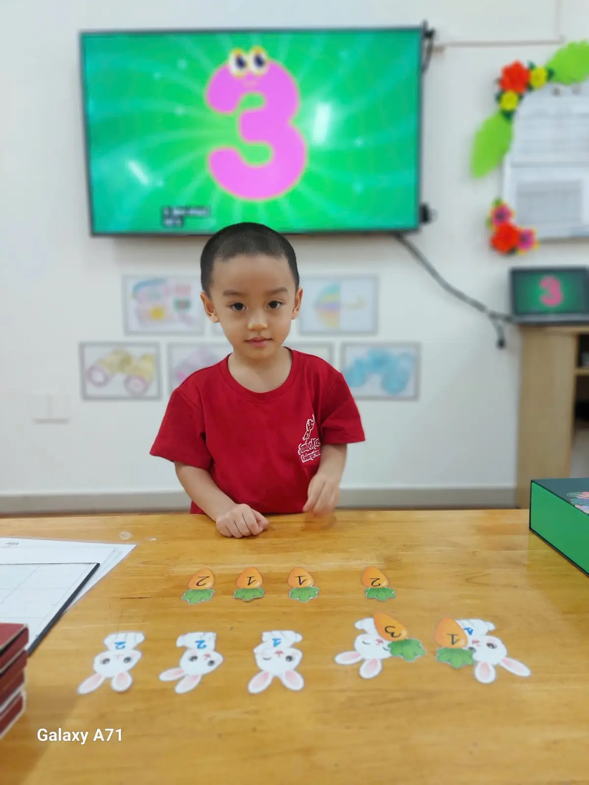 Bé trai lớp Mầm K1 ngồi trước bảng ghép số có hình cà rốt và thỏ