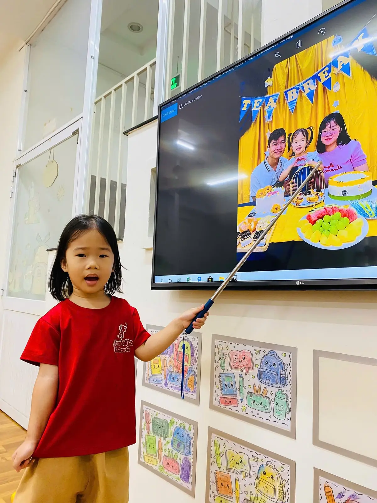 Bé gái lớp Mầm K1 vừa chỉ ảnh gia đình trên màn hình vừa kể cho các bạn nghe