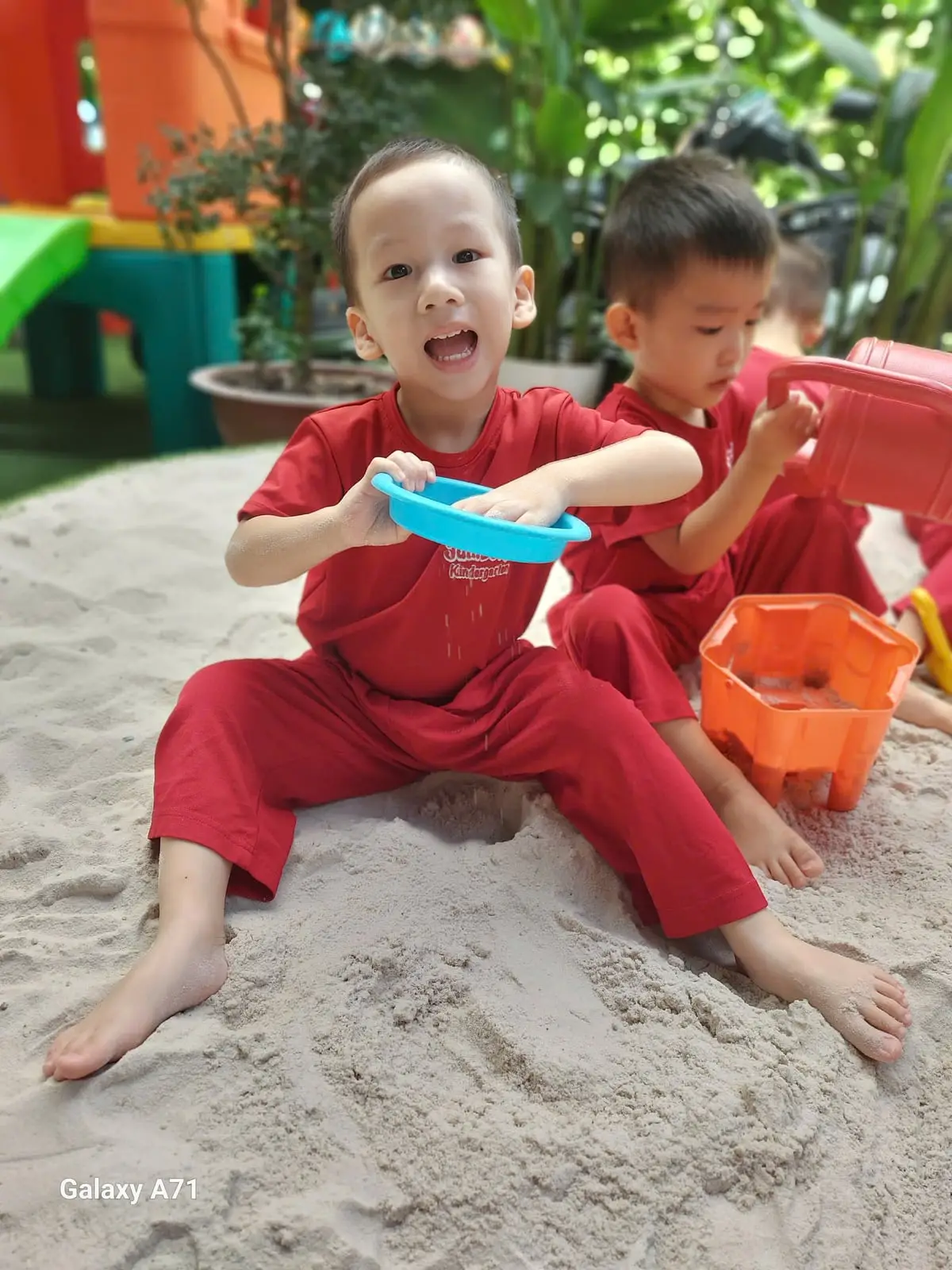 Bé trai lớp Mầm K1 hớn hở rắc cát qua rây xanh cùng bạn trong giờ Jumbo Gym