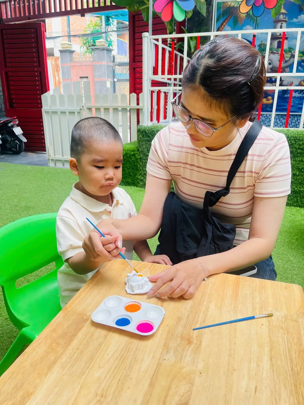 Mẹ cầm tay bé trai cùng tô màu tượng thạch cao, ba mẹ đồng hành cùng con