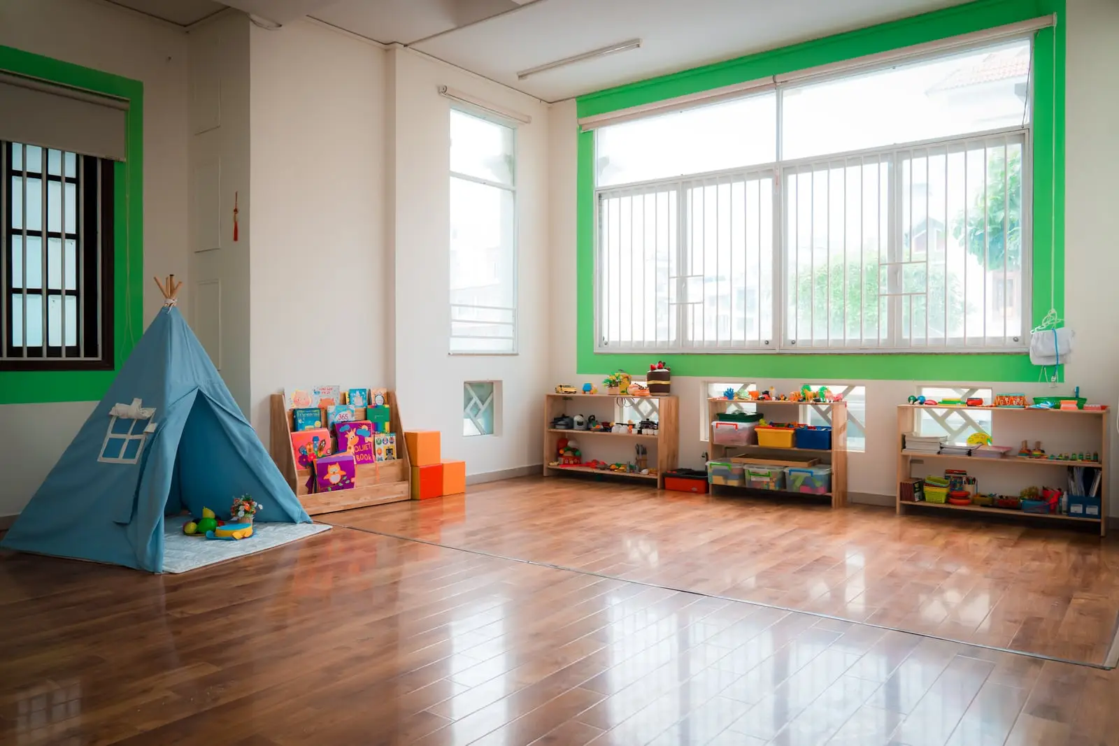 Phòng học sàn gỗ có lều đọc sách và kệ đồ chơi